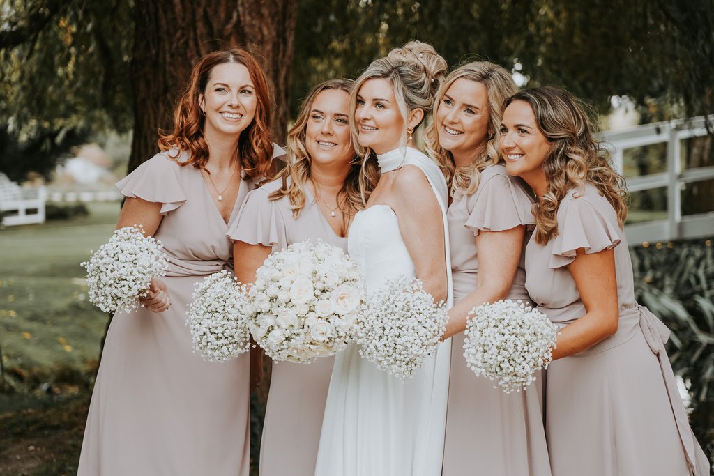A bride laughing with her bridesmaids, each holding gypsophila bouquets