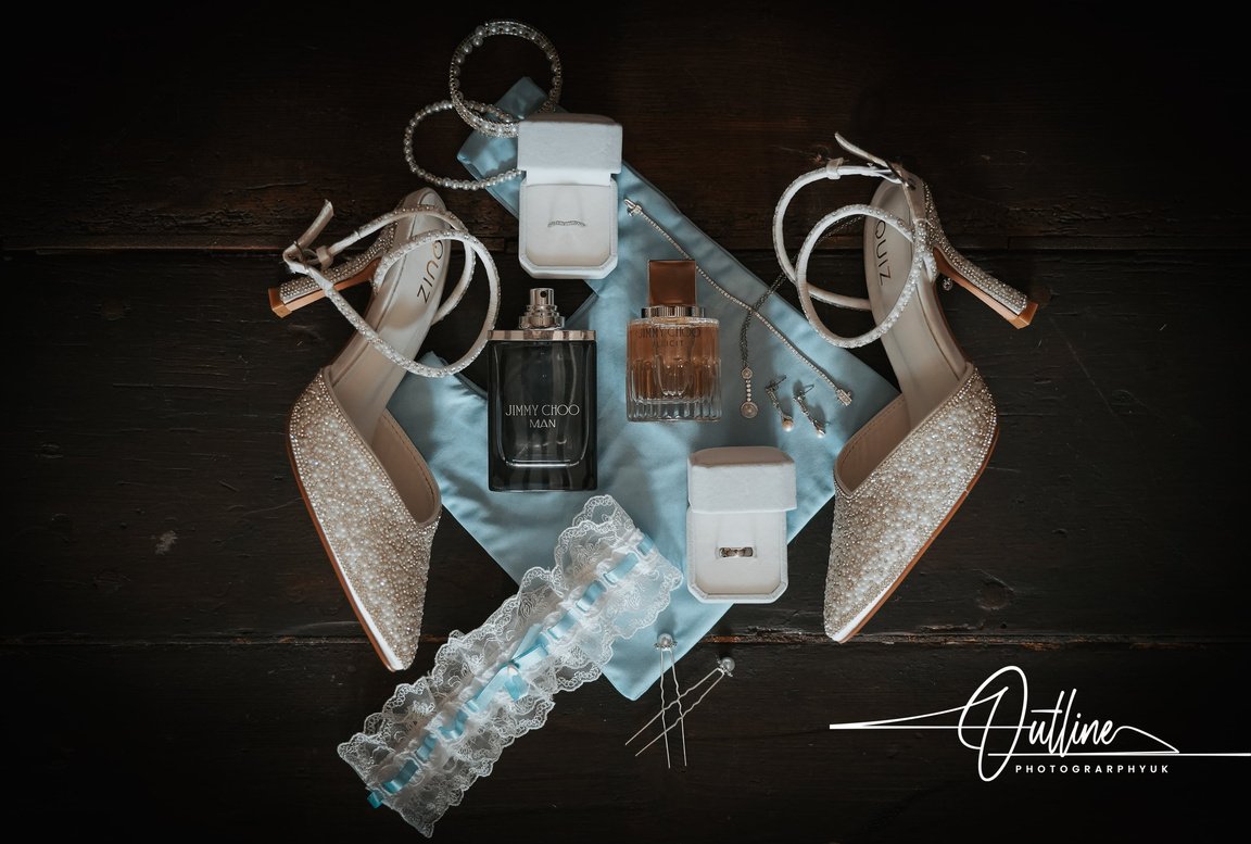 Bridal details flat lay: jewelled heels, perfume, ring box and a lace garter
